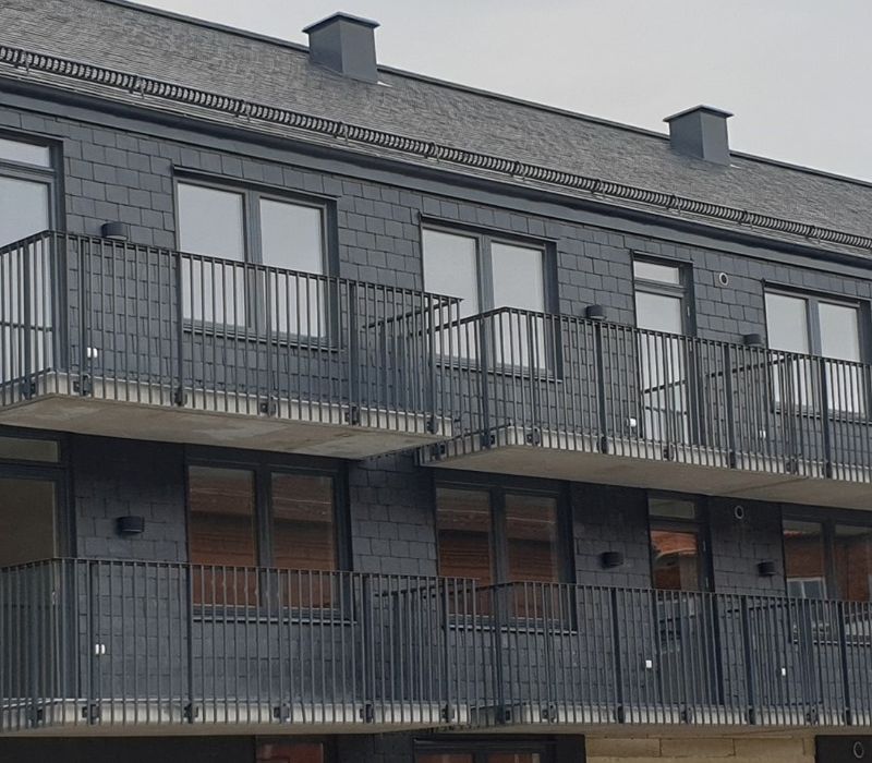 Flerbostadshus med mörk plåtfasad, svarta balkongräcken och fönster i rad.